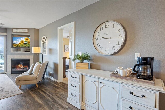 interior space featuring dark wood-style flooring, a tiled fireplace, baseboards, and visible vents