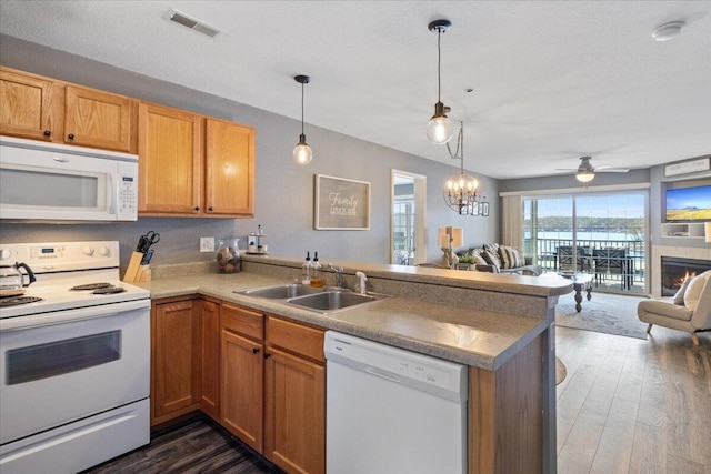 kitchen with white appliances, a sink, a peninsula, open floor plan, and dark wood-style floors