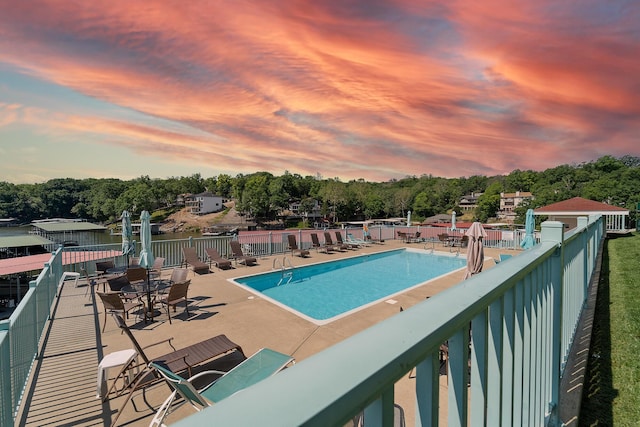 pool at dusk featuring fence, a patio, and a community pool