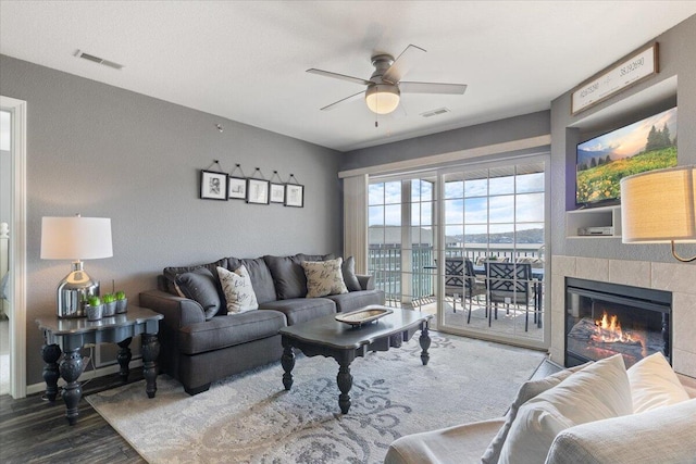 living area with a tile fireplace, visible vents, wood finished floors, and ceiling fan