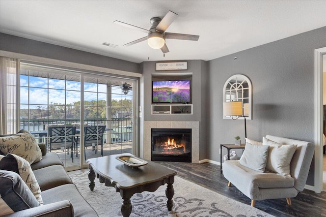 living area featuring wood finished floors, visible vents, a ceiling fan, baseboards, and a tiled fireplace