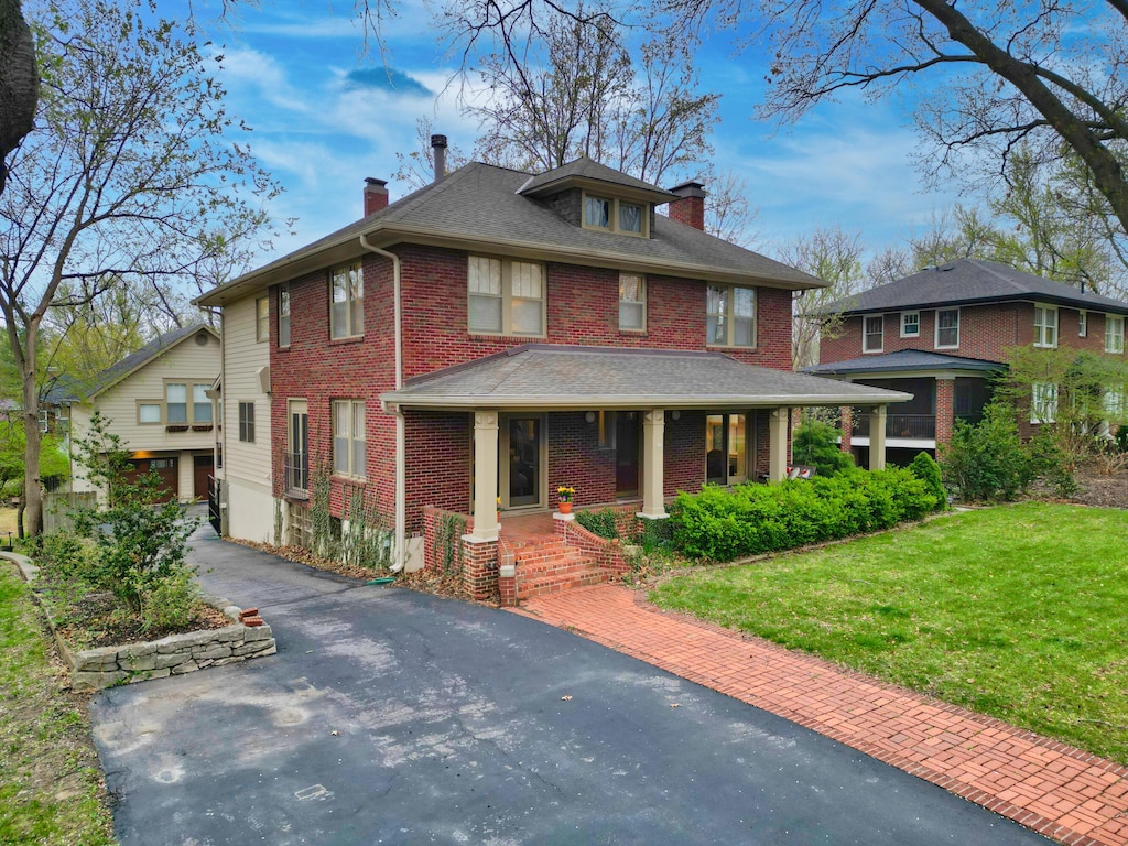 american foursquare style home featuring brick siding, driveway, a chimney, and a front lawn