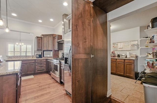 kitchen featuring tasteful backsplash, a peninsula, a chandelier, appliances with stainless steel finishes, and light stone counters