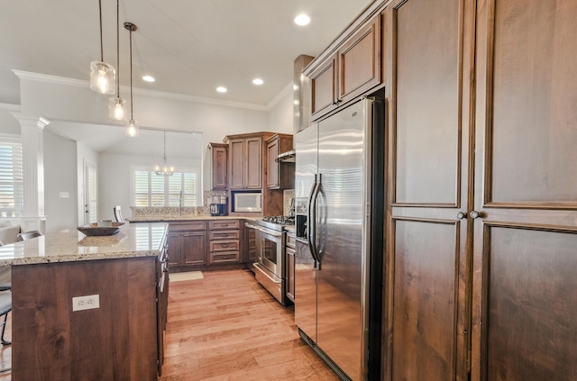 kitchen with ornamental molding, light wood-type flooring, light stone countertops, pendant lighting, and stainless steel appliances