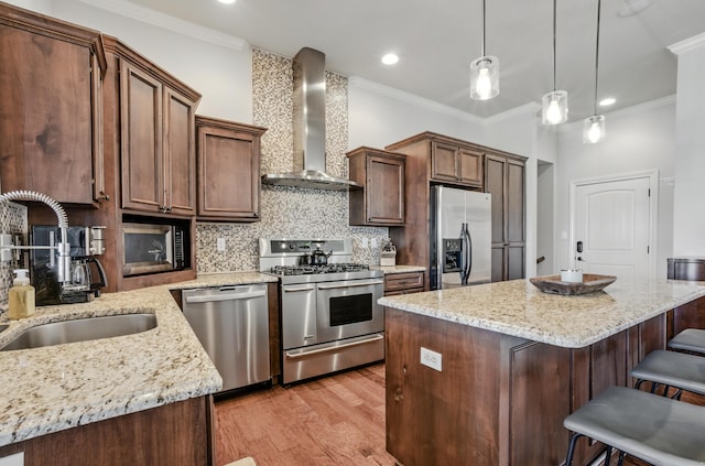 kitchen featuring tasteful backsplash, crown molding, wall chimney exhaust hood, appliances with stainless steel finishes, and a sink
