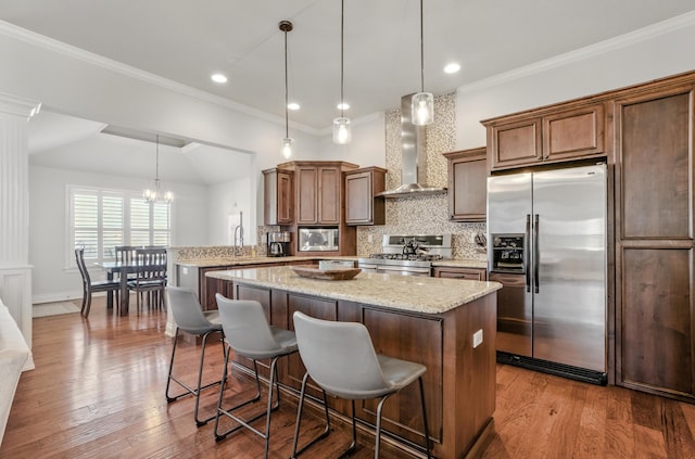 kitchen with wall chimney range hood, light stone countertops, backsplash, a kitchen island, and stainless steel appliances
