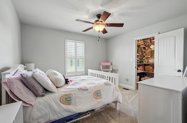 bedroom with visible vents, baseboards, a ceiling fan, a walk in closet, and light carpet