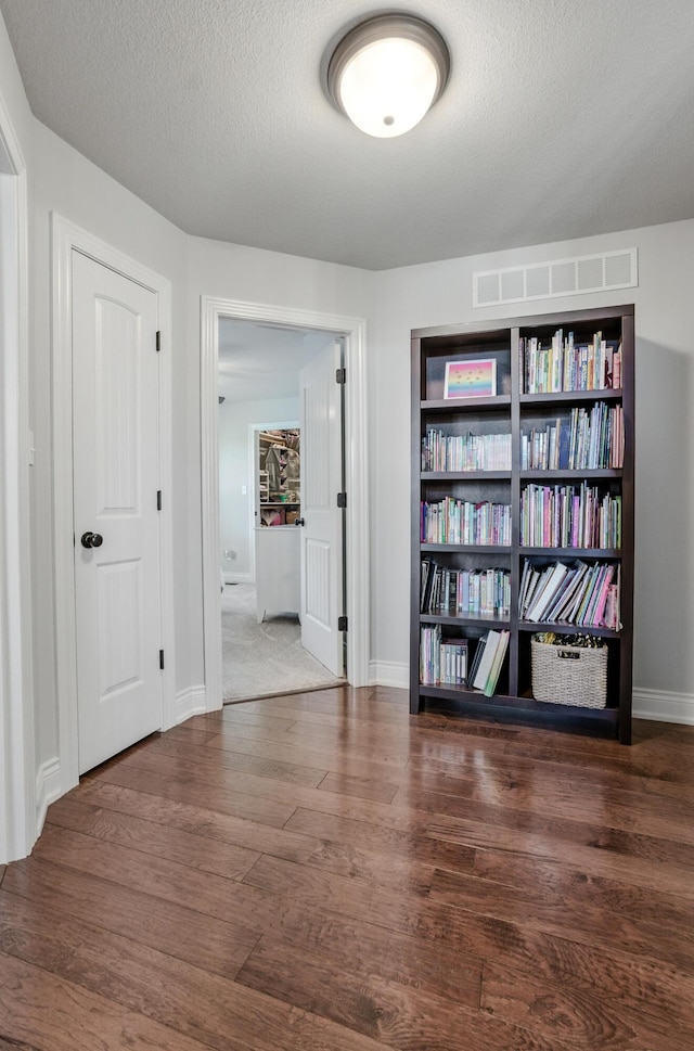 corridor featuring a textured ceiling, wood finished floors, baseboards, and visible vents