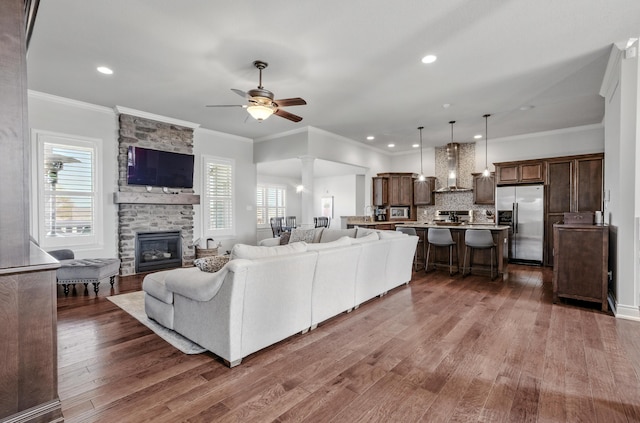 living area featuring a stone fireplace, ornamental molding, recessed lighting, a ceiling fan, and dark wood-type flooring