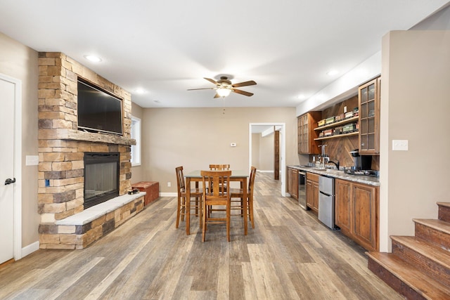 dining area featuring indoor wet bar, a ceiling fan, a stone fireplace, wood finished floors, and beverage cooler