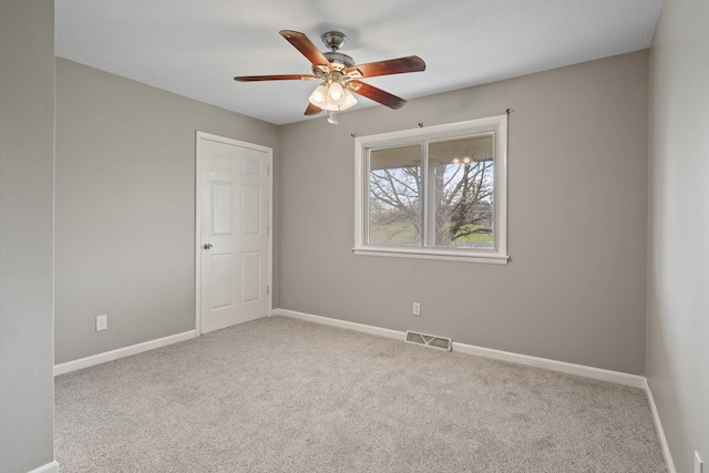 spare room featuring carpet floors, visible vents, baseboards, and ceiling fan