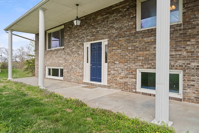 doorway to property featuring brick siding, a lawn, and a patio