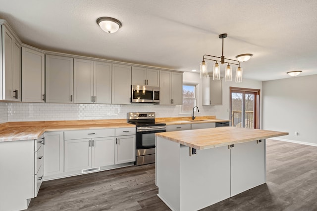 kitchen with dark wood-style floors, stainless steel appliances, backsplash, a sink, and wood counters