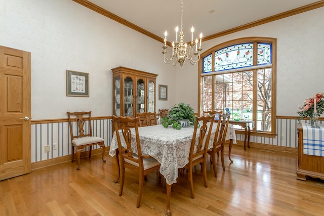 dining room featuring a high ceiling, wallpapered walls, a notable chandelier, light wood-style floors, and ornamental molding