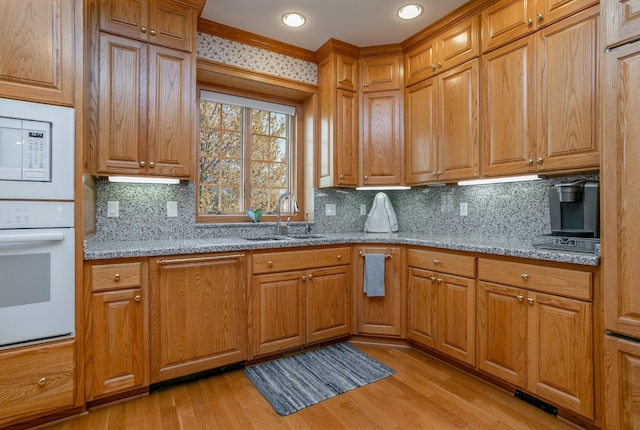 kitchen featuring a sink, light wood finished floors, light stone countertops, and white appliances