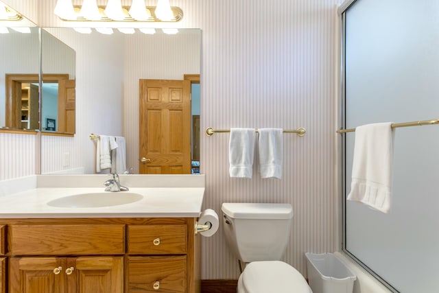 bathroom featuring vanity, toilet, bath / shower combo with glass door, and wallpapered walls