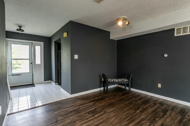 foyer entrance with visible vents, baseboards, wood finished floors, and a textured ceiling