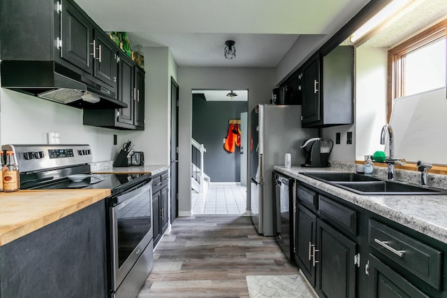 kitchen featuring under cabinet range hood, dishwasher, a sink, light wood-style flooring, and stainless steel range with electric stovetop