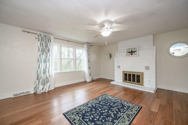 unfurnished living room with wood finished floors, visible vents, a fireplace, and ceiling fan