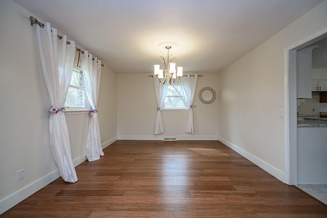 unfurnished dining area with visible vents, baseboards, wood finished floors, and a chandelier