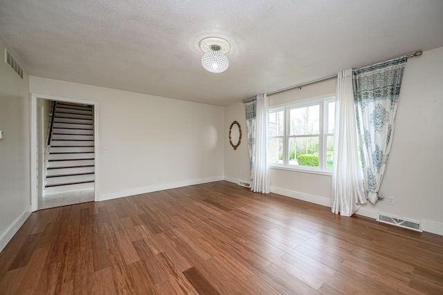 spare room featuring stairs, wood finished floors, visible vents, and a textured ceiling