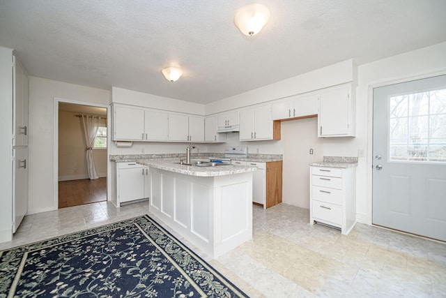 kitchen with electric stove, a sink, a textured ceiling, white cabinets, and under cabinet range hood