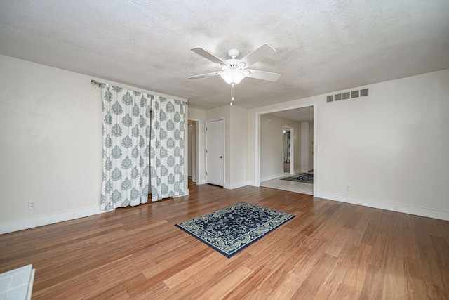 unfurnished room with a textured ceiling, baseboards, visible vents, a ceiling fan, and wood finished floors