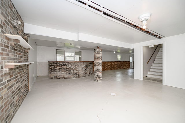 basement featuring stairway, a wainscoted wall, and brick wall