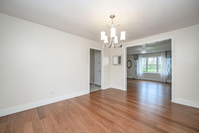 unfurnished room featuring baseboards, a notable chandelier, and wood finished floors