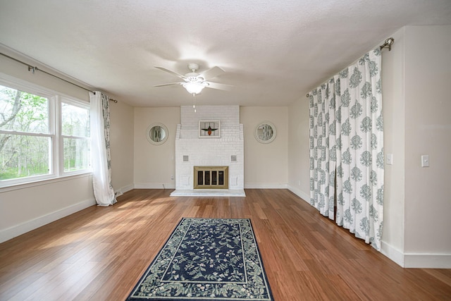 unfurnished living room featuring baseboards, a ceiling fan, a brick fireplace, and light wood finished floors