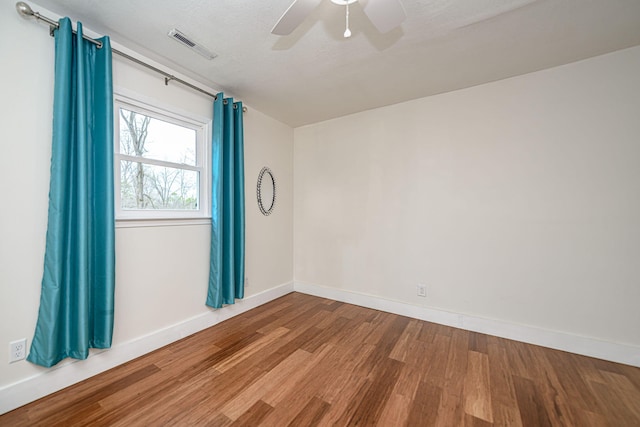 unfurnished room with wood finished floors, visible vents, a ceiling fan, and baseboards