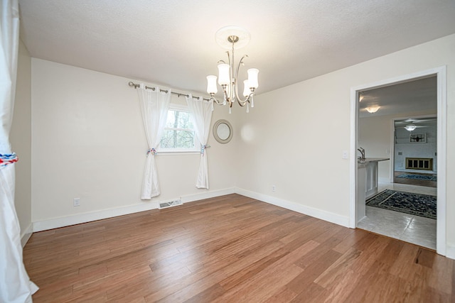 unfurnished dining area with a textured ceiling, baseboards, visible vents, ceiling fan with notable chandelier, and wood finished floors