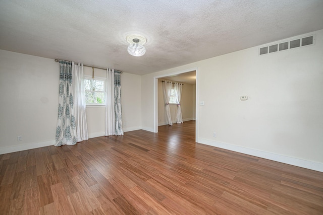 unfurnished room featuring baseboards, wood finished floors, a textured ceiling, and visible vents