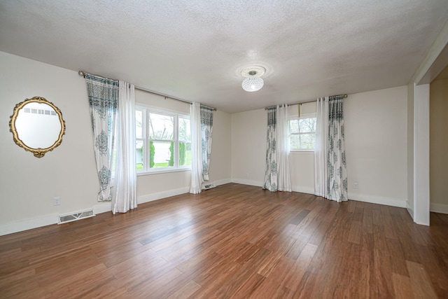 unfurnished room with plenty of natural light, wood finished floors, visible vents, and a textured ceiling