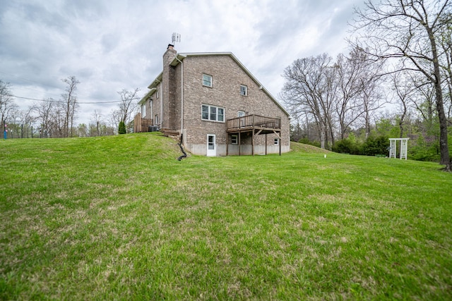back of property with a wooden deck, a lawn, a chimney, and brick siding