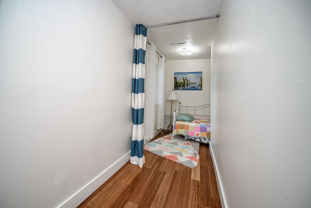 corridor featuring wood finished floors, a textured ceiling, and baseboards