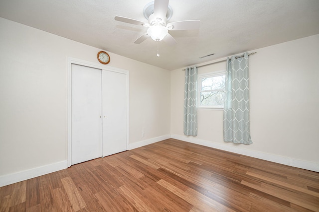 unfurnished bedroom featuring baseboards, a ceiling fan, wood finished floors, and a closet