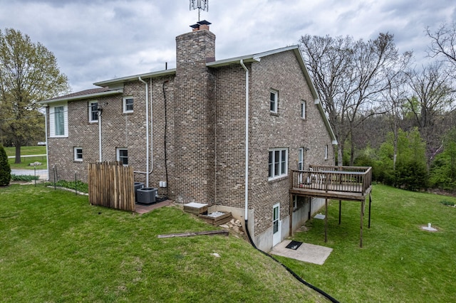 back of house with a chimney, central AC unit, a wooden deck, a lawn, and brick siding