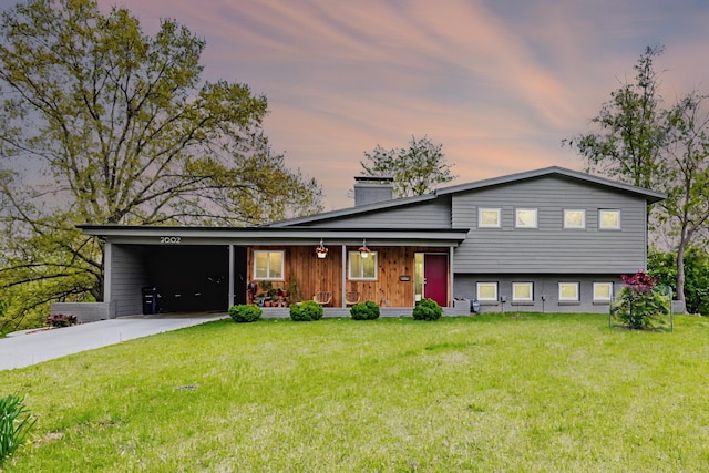 tri-level home with a chimney, an attached carport, driveway, a yard, and covered porch