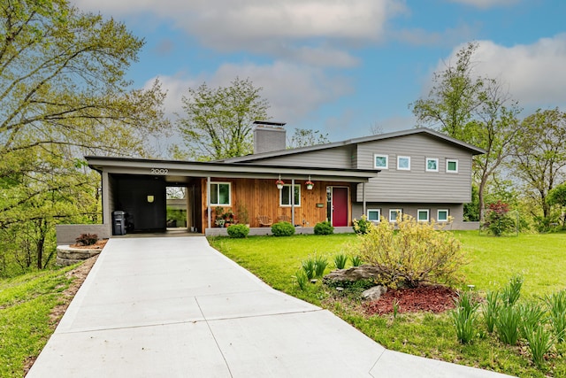 split level home with concrete driveway, a chimney, a carport, and a front lawn