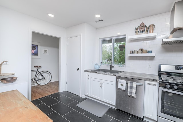 kitchen featuring appliances with stainless steel finishes, a sink, wall chimney range hood, white cabinetry, and backsplash