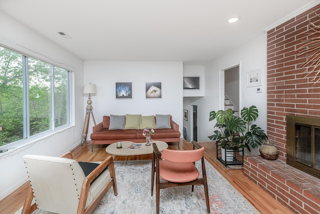 living area with light wood finished floors, baseboards, a brick fireplace, stairway, and recessed lighting