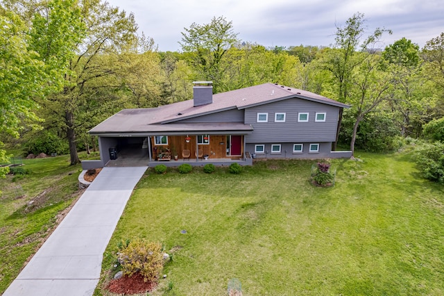 view of front of home with a view of trees, driveway, a front lawn, a chimney, and a porch
