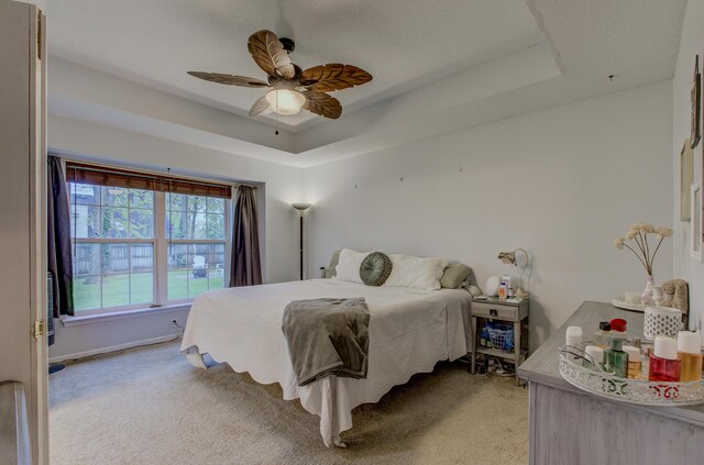 bedroom with baseboards, a ceiling fan, a tray ceiling, and light carpet