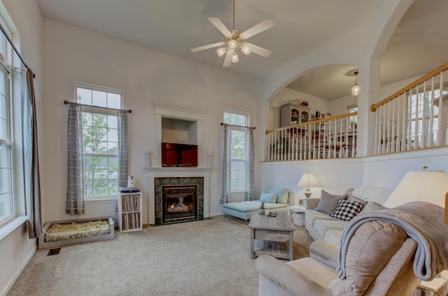 living area with carpet floors, a ceiling fan, arched walkways, and a tile fireplace