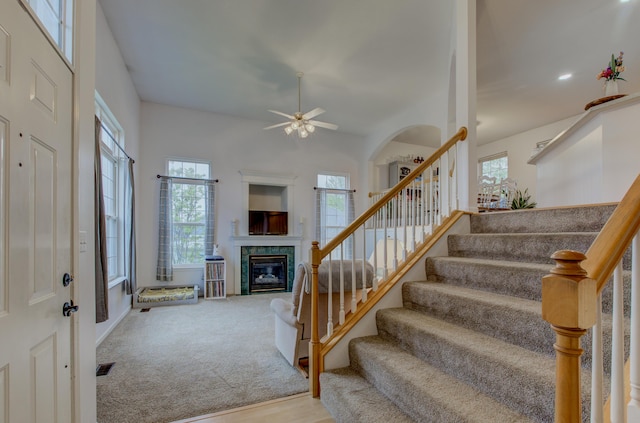 staircase featuring ceiling fan, plenty of natural light, carpet, and a fireplace