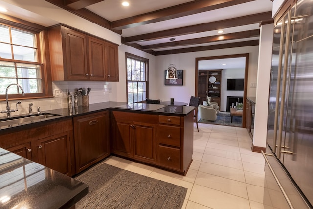 kitchen featuring a sink, decorative backsplash, light tile patterned flooring, a peninsula, and beamed ceiling