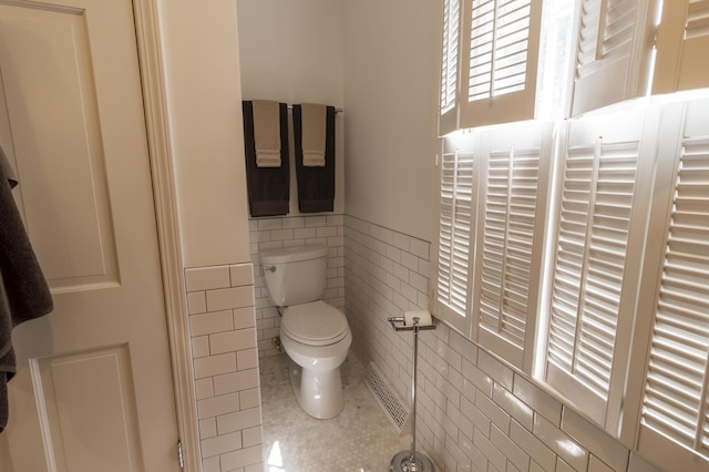 bathroom with tile walls, tile patterned flooring, toilet, and a wainscoted wall
