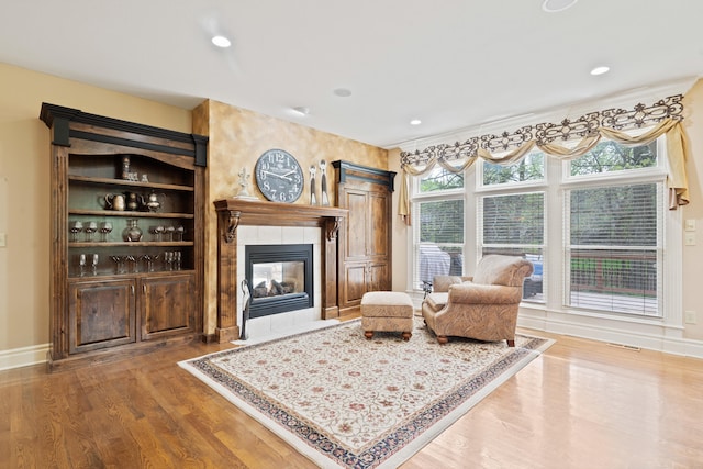 living room featuring a tile fireplace, baseboards, wood finished floors, and recessed lighting