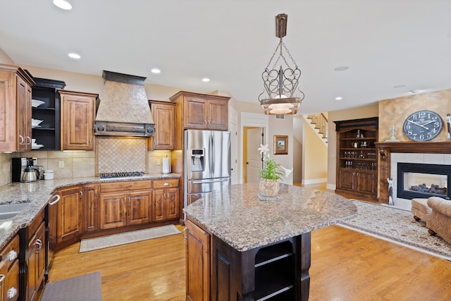 kitchen with open shelves, appliances with stainless steel finishes, a kitchen island, light wood finished floors, and custom exhaust hood